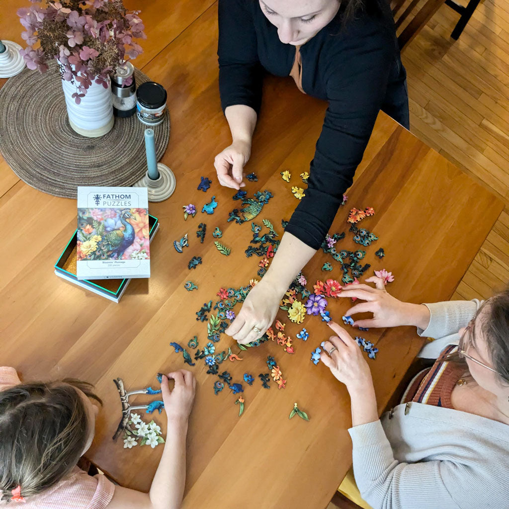 Fathom Puzzles Bloomin' Plumage Wooden Laser Cut Jigsaw 200 Pieces Geoff Cota People putting pieces together on table