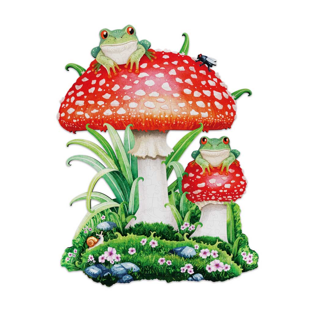 Completed wooden jigsaw puzzle showing two red-capped toadstools with white spots, each topped by a green tree frog, set in a grassy bed of pink flowers, rocks, and a snail, with a fly perched on the larger mushroom cap.