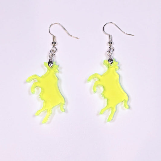A pair of neon green translucent acrylic cow-shaped earrings with silver hooks, laid flat against a light lavender background. The cow silhouettes are slightly irregular with organic edges, and cast soft shadows beneath them.