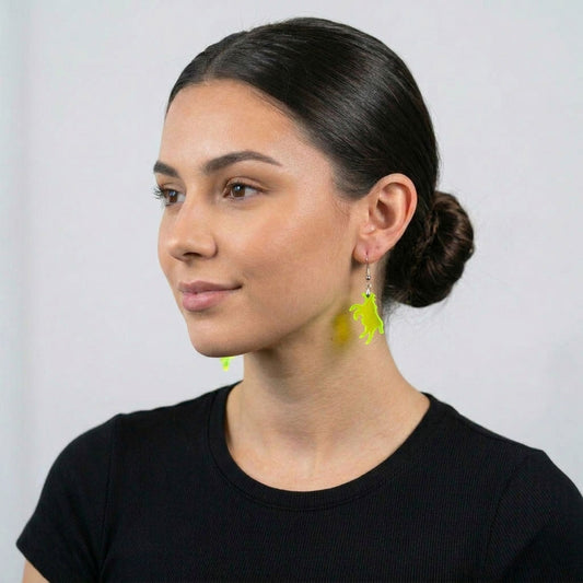 The same woman photographed from a three-quarter angle, looking to her left. The neon green acrylic cow earring on her right ear is clearly visible in profile, showing the dangle length against her neck and the silver hook hardware.