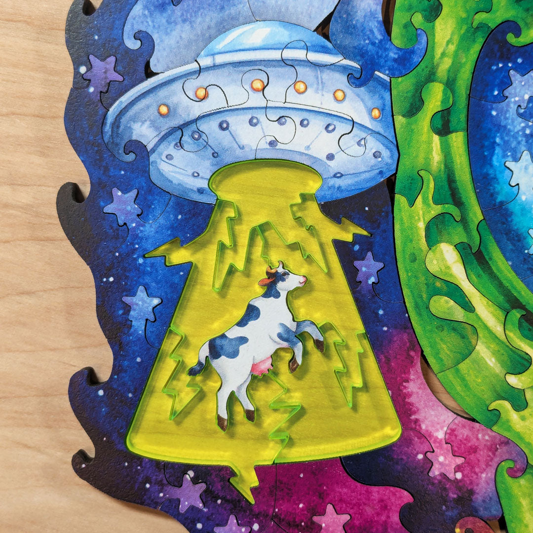 Close-up of the UFO and tractor beam section, featuring neon green acrylic pieces forming the tractor beam with a laser-cut cow suspended inside it beneath a detailed flying saucer.
