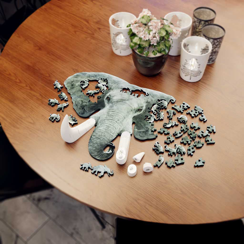 Close-up side view of the puzzle on a table, highlighting the tall, freestanding white tusk pieces rising above the flat elephant face.