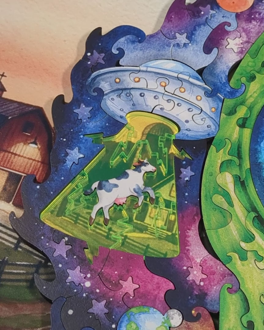 A neon green acrylic surrounding cow puzzle piece appears to float and fly as a starry night sky slowly scrolls beneath it, visible through the transparent acrylic. The effect gives the impression the cow is soaring through space, mid-abduction.